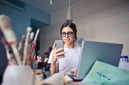 mujer viendo celular mientras trabaja en computadora