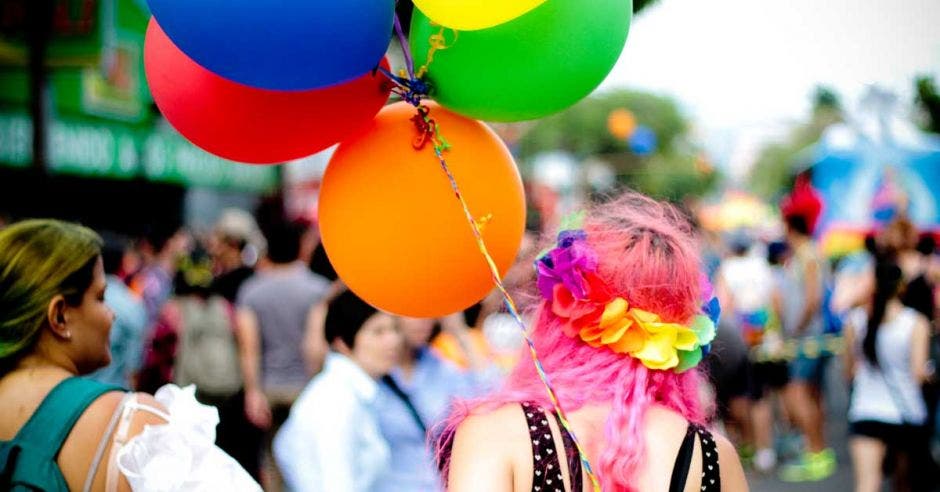 Joven de cabello rosa está de espalda sosteniendo unos globos de colores en la marcha