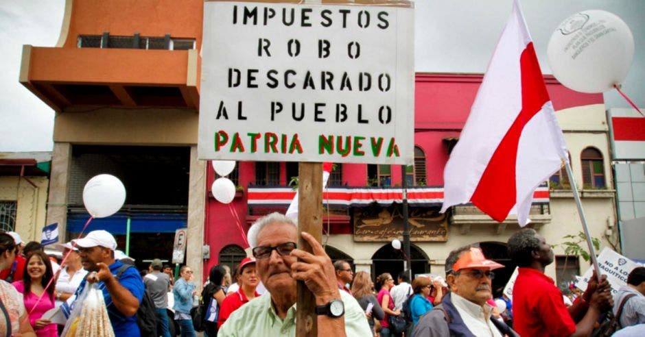 Un hombre sostiene una pancarta con una leyenda en contra de nuevos impuestos