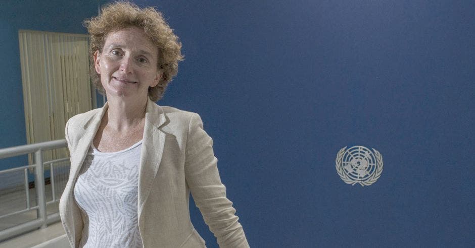 Alice Schackelford, coordinadora residente de la ONU, posa junto al logo de la ONU sobre un fondo azul