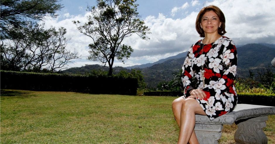 Laura Chinchilla sentada en un banco a campo abierto.