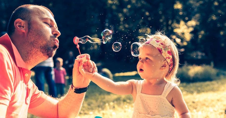 un hombre juega con su hija al hacer pompas de jabón