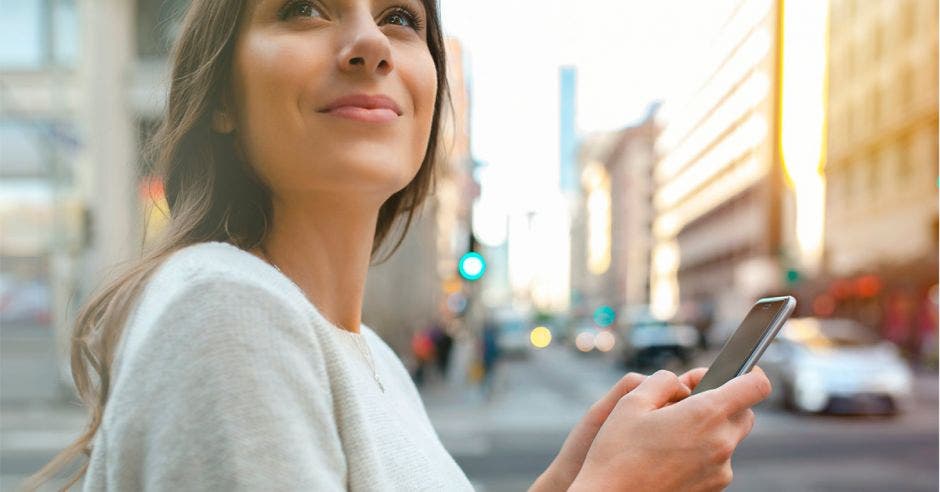 Una mujer sostiene un celular en una ciudad.