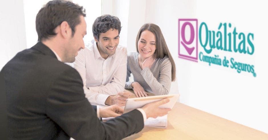 tres personas viendo algo en una tablet, atrás logo de Quálitas