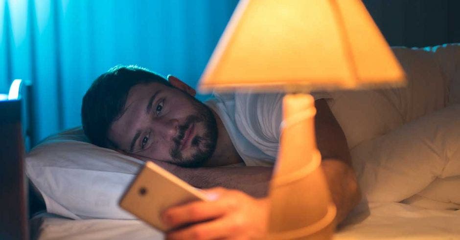 Un hombre mira su celular a la luz de una lámpara.