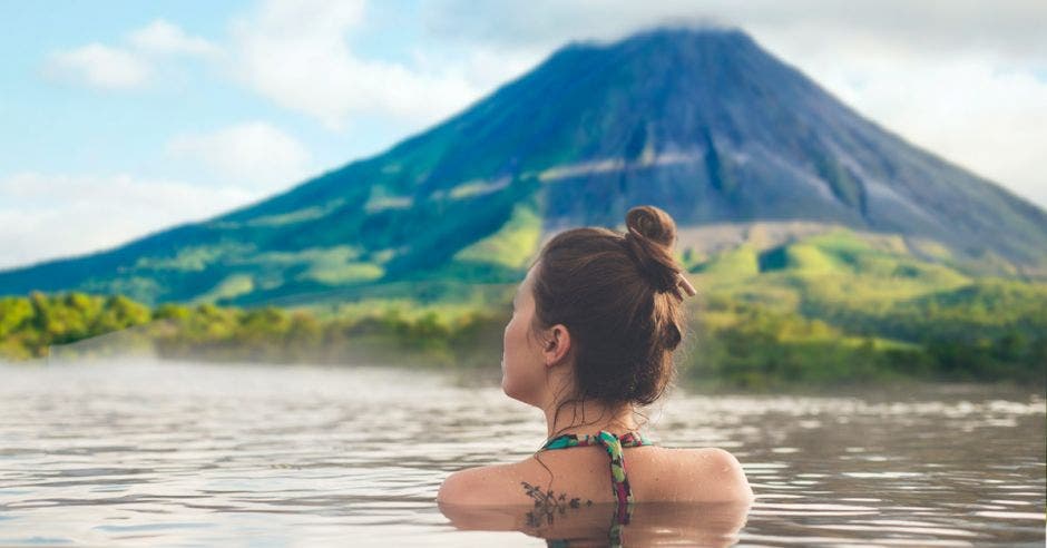 mujer en aguas termales mirando un volcán