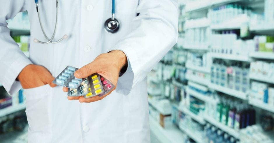 medico mostrando varios tipos de pastillas y de fondo la farmacia