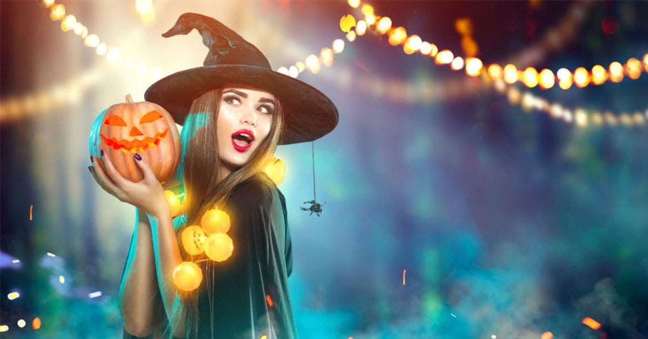 Una joven bruja de ojos claros, cabello alisado con una berenjena de halloween en su mano