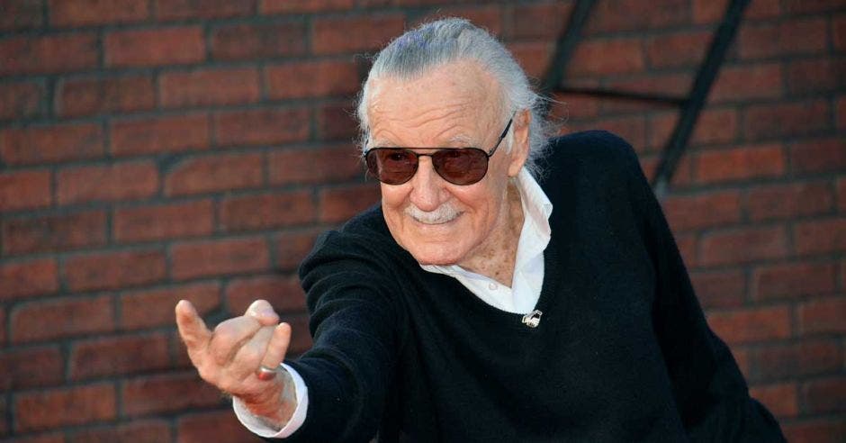 Stan Lee haciendo una señal con sus manos, vestido de negro