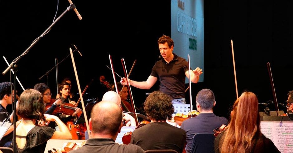 El director Paolo Bortolameolli con una camisa casual dando instrucciones frente a la orquesta