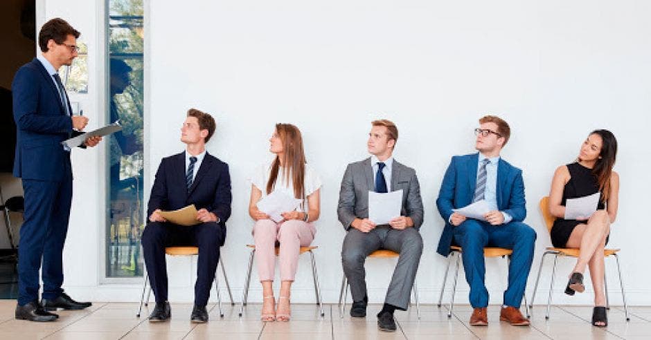 Tres hombres y dos mujeres vestidos formal, escuchan las instrucciones de un entrevistador