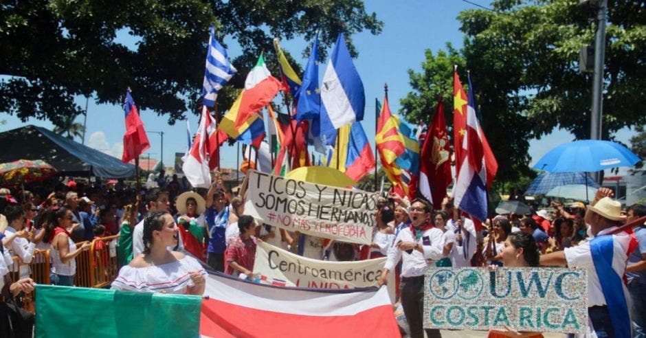 Varios niños vestidos con trajes tradicionales costarricenses con banderas de diferentes países y pancartas que dicen ticos y nicas somos hermanos