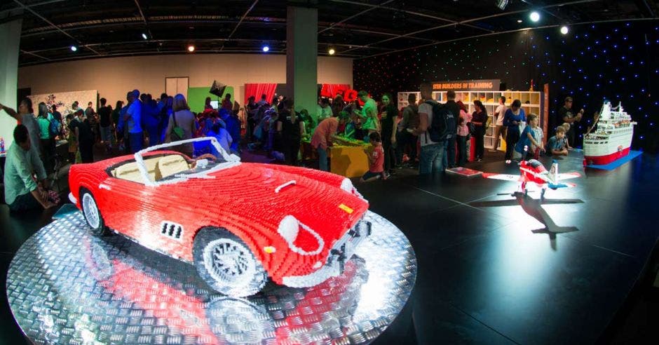 Un carro, un avión y un barco de legos en una exposición frente a decenas de personas