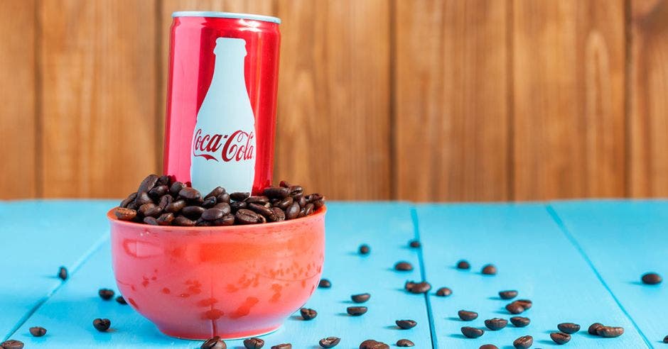 Un envase de coca cola sobre un tazón lleno de granos de café