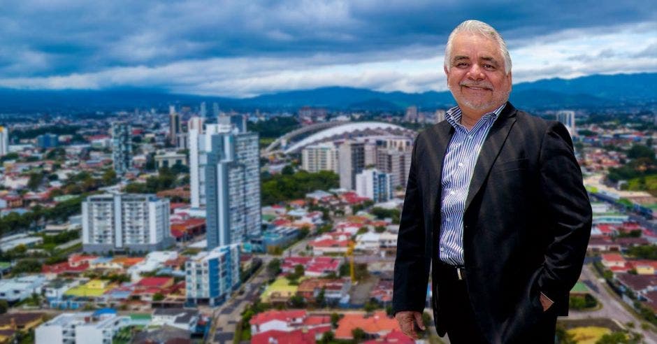 Un hombre posa, frente a un cartel de San José en donde se ve toda la ciudada