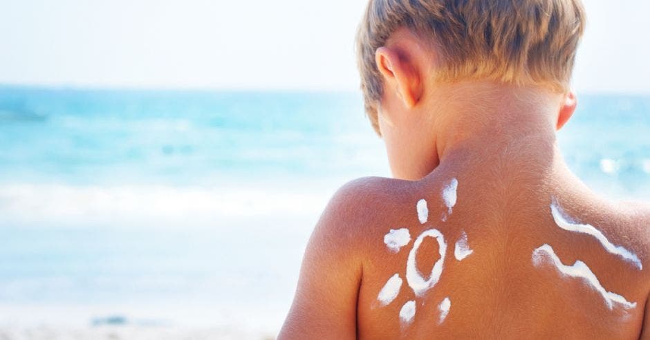 Un niño en la playa con bloqueador solar colocado en su espalda
