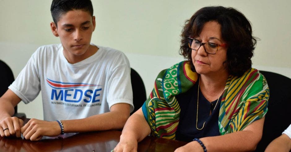 Un estudiante y Guiselle Cruz, ministra de Educación firmando un acuerdo
