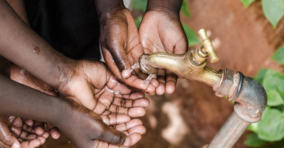 Manos de niños africanos tratando de rescatar agua de una tubería