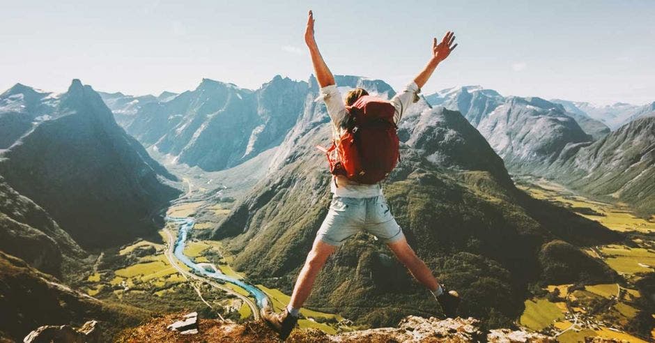 hombre con una mochila en la espalda saltando, de fondo una montaña