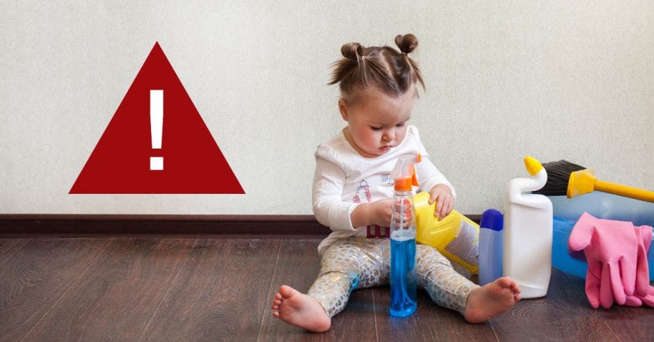 Una niña jugando con productos de limpieza y un símbolo de alerta