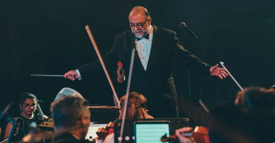 El director de la Filarmónica en medio del escenario dando instrucciones a la orquesta