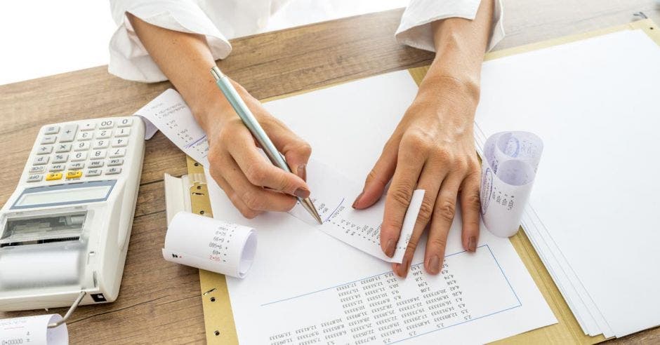 Persona escribiendo y sacando cuentas con un bolígrafo, en papel