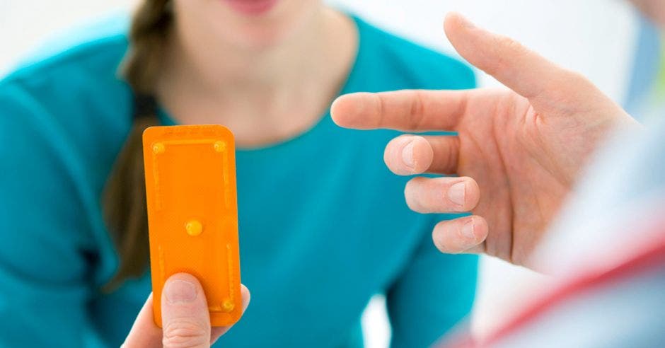 Una joven en una consulta médica y un doctor dándole una pastilla anticonceptiva de emergencia