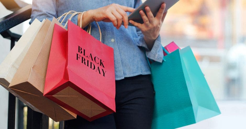 mujer cargando bolsas de compras de color café, verde y rosada que dice black friday.