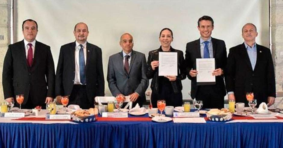 Seis personas frente una mesa d etrabajo, dos de las cuales sostienen el convenio firmado en sus manos.