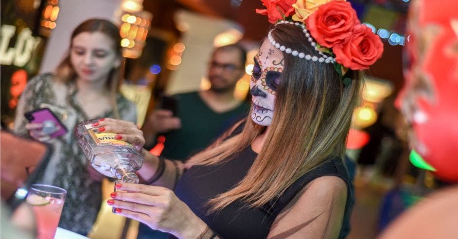 Mujer pintada de Catrina sirviendo tequila