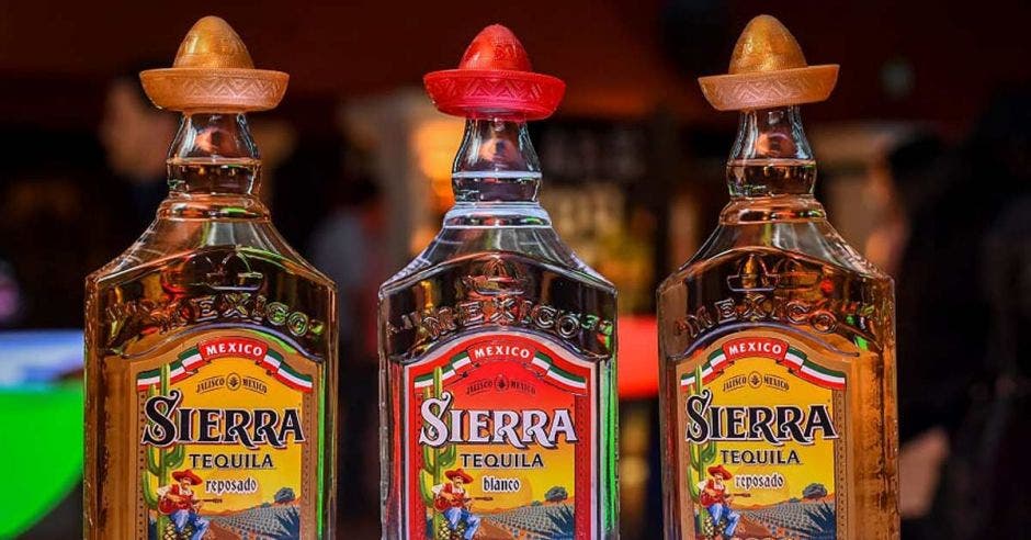 Tres de las botellas tequilas que ofrece la marca en amarillo y rojo las etiquetas, con una sombrero mexicano en la tapa