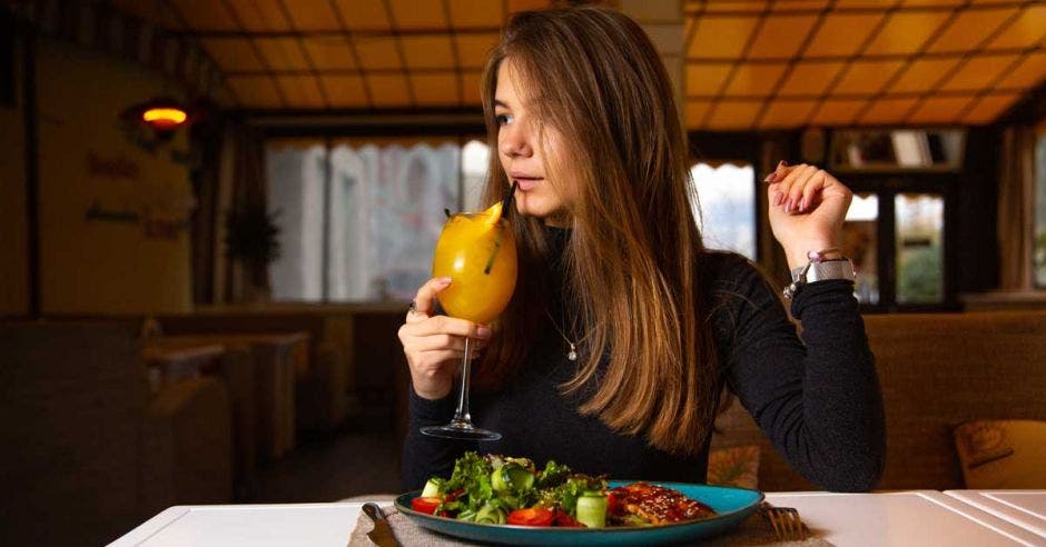 Una mujer disfruta de una mimosa y un platillo de carne con ensalada