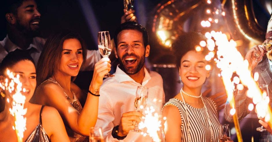 Varias personas disfrutando de una fiesta con copas de champagne y juegos artificiales