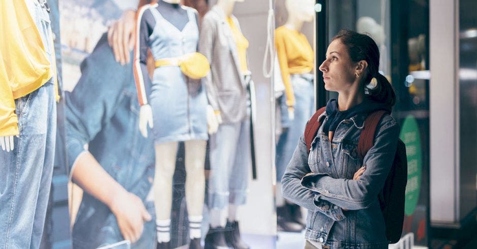 Mujer observa una ventana de una tienda de ropa con una expresión triste