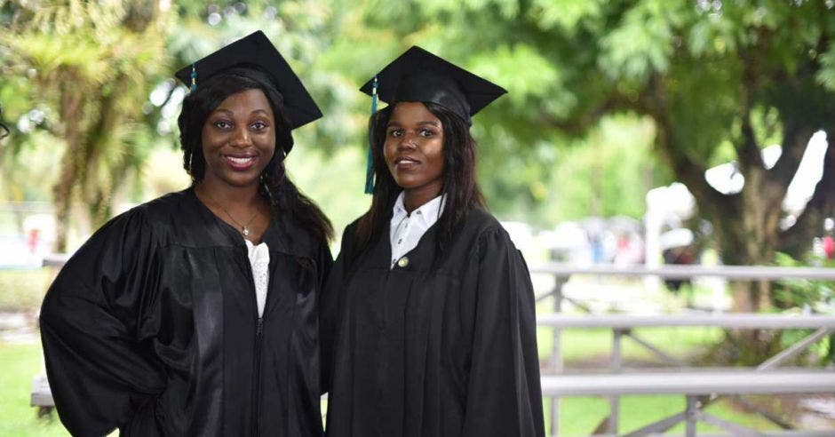 Dos mujeres con un birrete negro sonrientes frente a la cámara