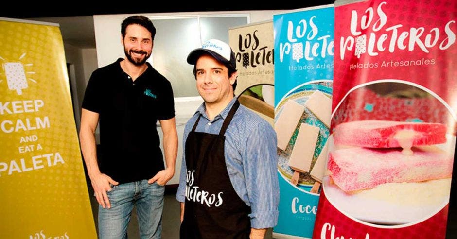 Dos hombres jóvenes posan frente a banners de los paleteros