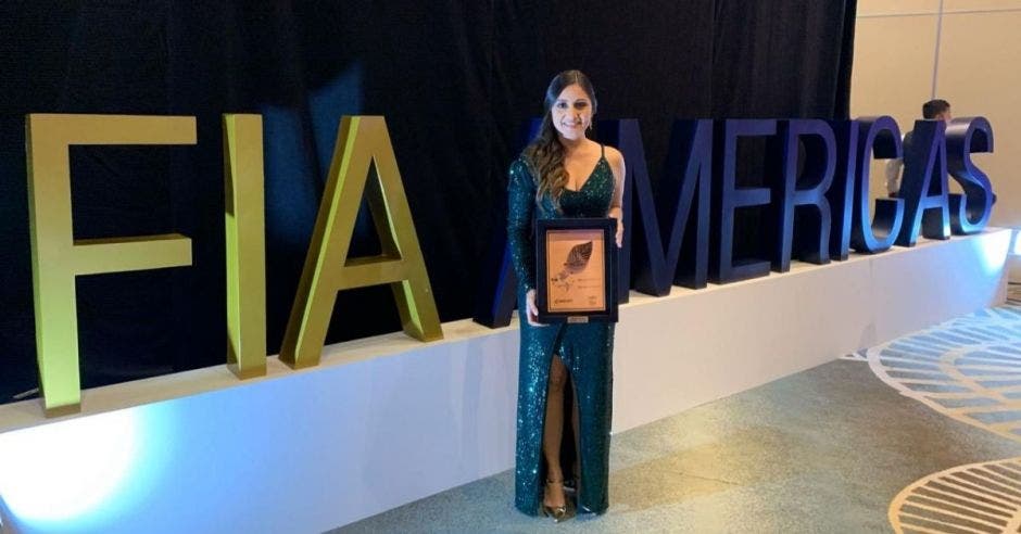 Una mujere con un vestido de gala verde posa frente a un letrero que dice FIA Americas