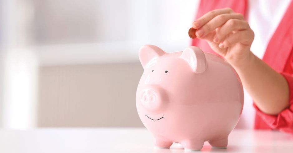 mujer echando una moneda en un chancho de alcancía