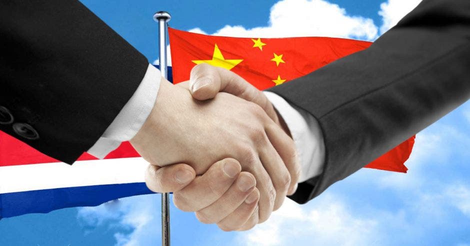 dos personas dándose la mano con banderas de Costa Rica y China de fondo