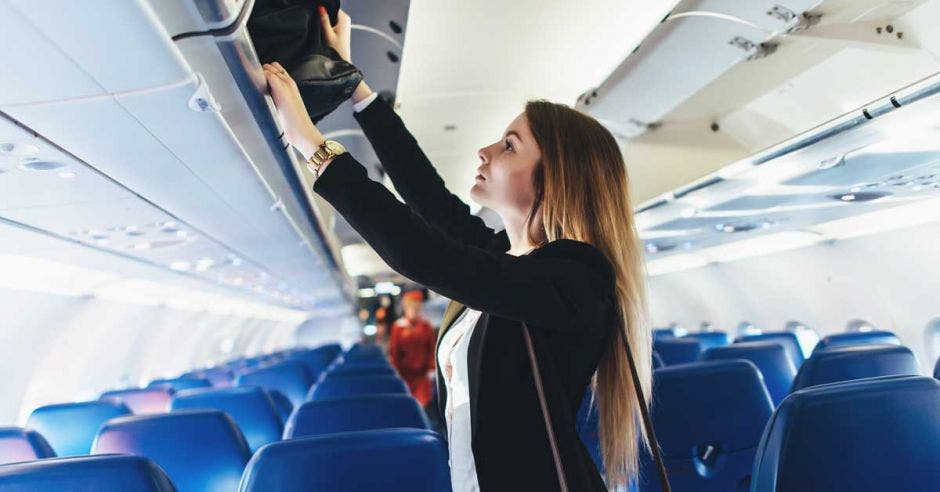 Estudiante colocando su equipaje de mano en un armario en el avión