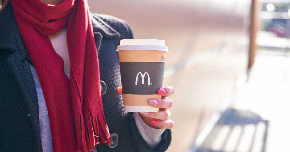 Una mujer con bufanda roja sostiene un café