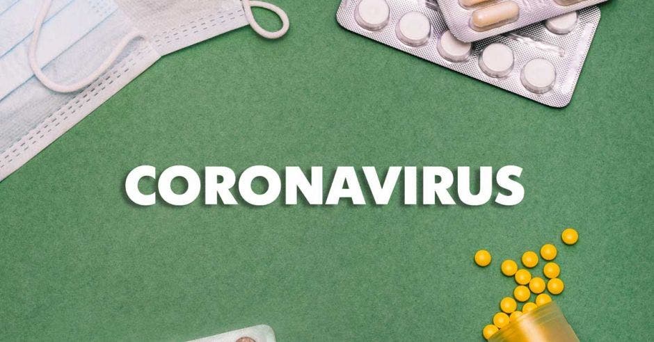 Una mascarilla, una serie de pastillas y tabletas sobre un fondo verde que tiene escrito con letras blancas la palabra coronavirus