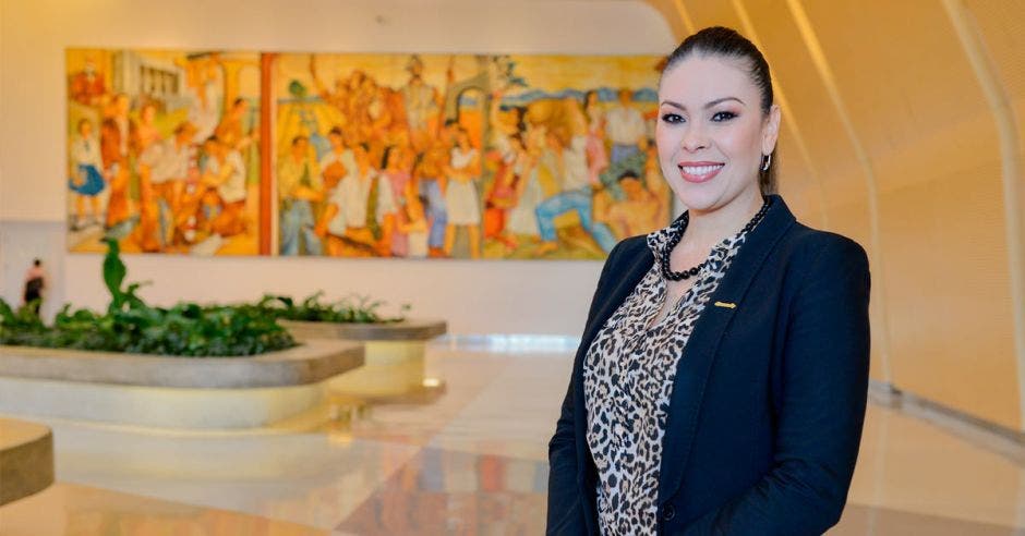 Una mujer sonriente en un lobby de hotel vistiendo un blazer azul y una blusa estampada