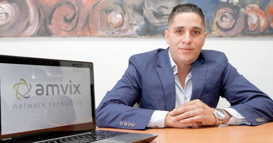 El director de Amvix, con traje entero en un escritorio y la computadora a un lado con el logo de la empresa Amvix