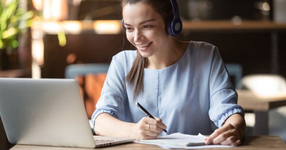 Una mujer tomando apuntes de una computadora con audífonos