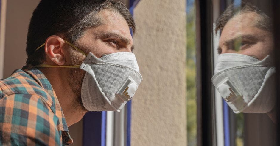 Un hombre con mascarilla mira por la ventana