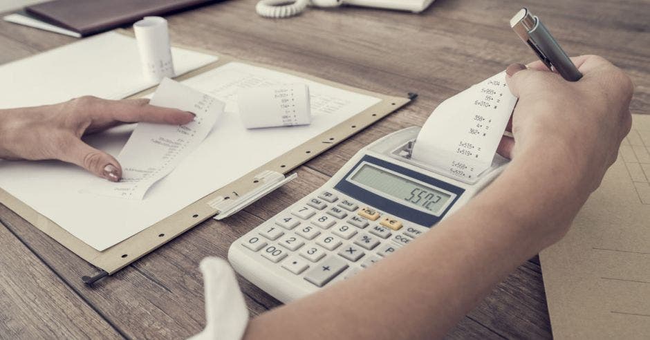 Persona con una calculadora  y un libro  sacando  cálculos