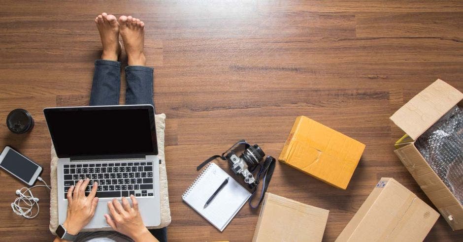 Una mujer sentada en el suelo consulta en su computadora detalles sobre comercio electrónico