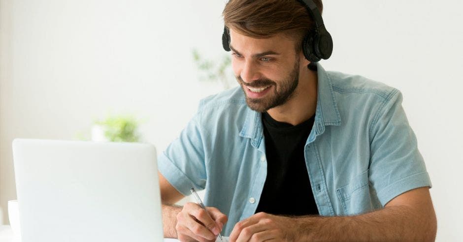 Un hombre de barba hace apuntes mientras mira su computadora