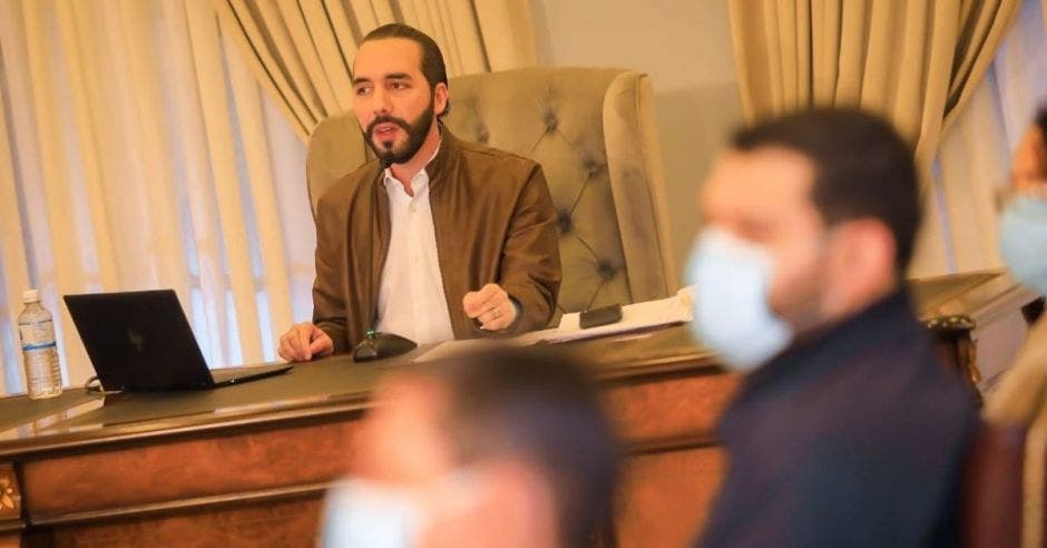 Un hombre de barba y pelo negro viste una chaqueta beige y camisa blanca